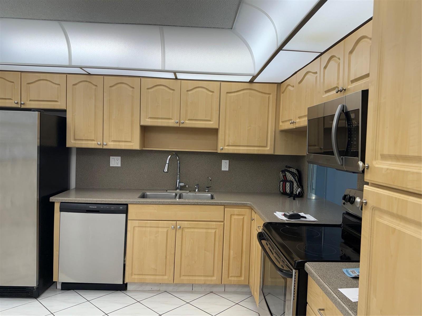 A kitchen featuring light wood cabinets, stainless steel appliances, and a gray countertop — 4930 E Sabal Palm Boulevard # 402, Tamarac FL 33319, TAMARAC, FL