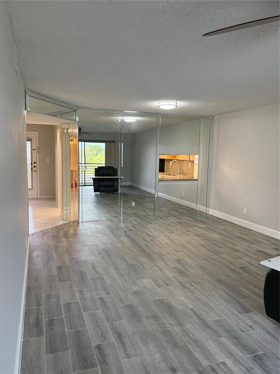 A living area features gray wood-look tile flooring and a large mirrored wall partition — 4930 E Sabal Palm Boulevard # 402, Tamarac FL 33319, TAMARAC, FL