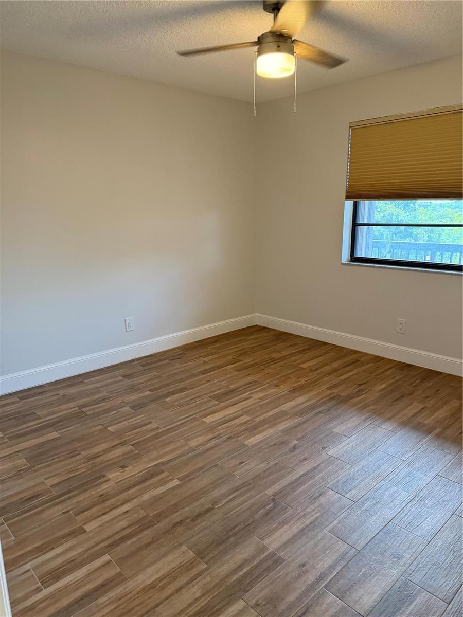 An empty bedroom features light-colored walls, wood-look tile flooring, a ceiling fan, and a window — 4930 E Sabal Palm Boulevard # 402, Tamarac FL 33319, TAMARAC, FL