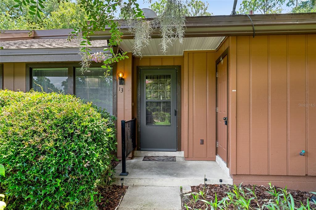 The exterior of a brown house features a front door, a window, and landscaping — 19660 SW 83RD PLACE ROAD UNIT C13, DUNNELLON, FL