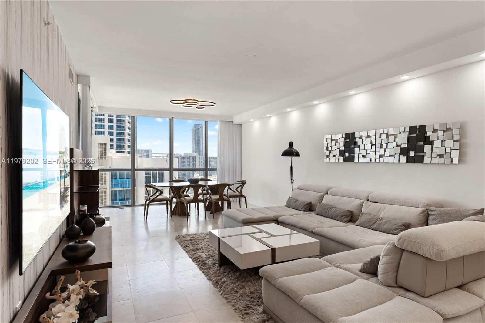 A modern living room features a large sectional sofa, a dining area, and floor-to-ceiling windows — 3101 S Ocean Dr # 1504, Hollywood FL 33019, HOLLYWOOD, FL