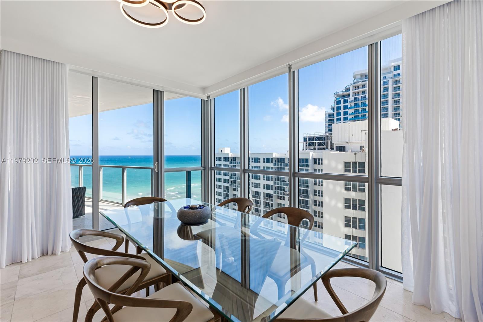 A dining room with a glass table, wooden chairs, and floor-to-ceiling windows overlooking the ocean — 3101 S Ocean Dr # 1504, Hollywood FL 33019, HOLLYWOOD, FL