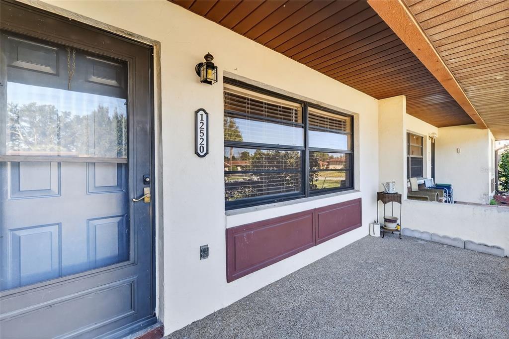 A covered concrete porch features a dark blue front door and a large window — 12520 ORANGEWOOD COURT, TAVARES, FL