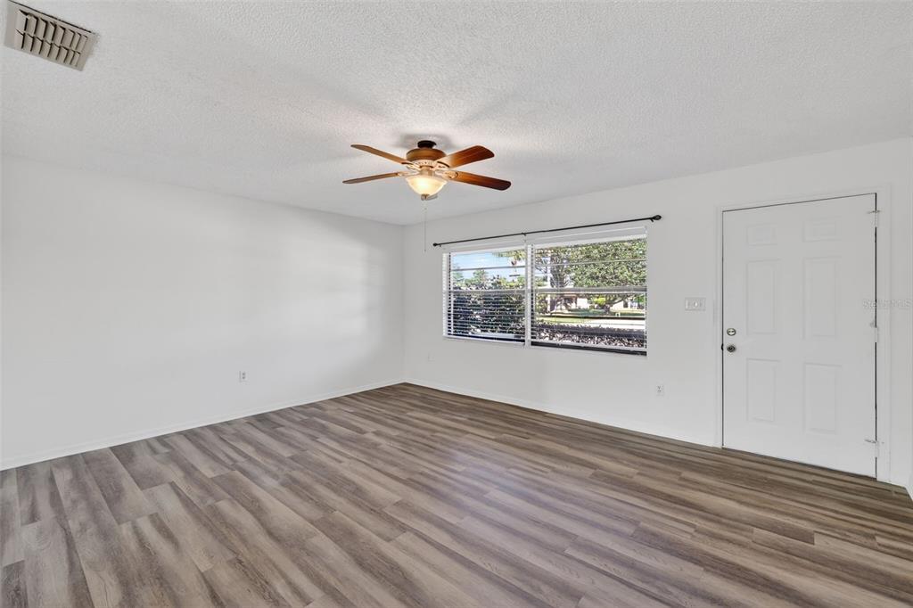 An empty living room features wood-look flooring, a ceiling fan, and a white front door — 12520 ORANGEWOOD COURT, TAVARES, FL