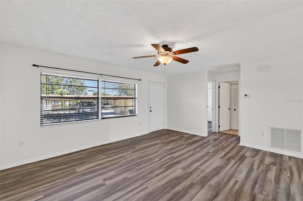 An empty living room features wood-look flooring, a ceiling fan, and a large window — 12520 ORANGEWOOD COURT, TAVARES, FL