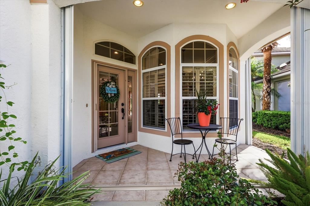 A covered patio features tiled flooring, a bistro set, and a glass-paneled front door — 3239 OSPREY LN, PORT CHARLOTTE, FL
