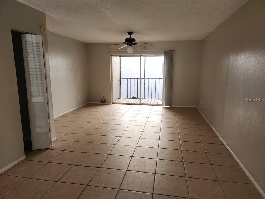 An empty living room with beige tile flooring, a ceiling fan, and a sliding glass door — 5507 POKEWEED COURT UNIT C, TAMPA, FL