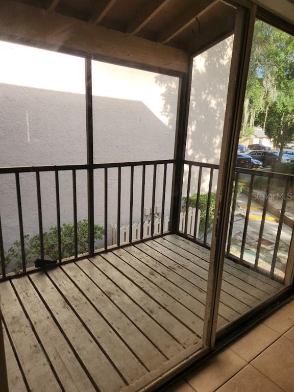 A screened-in balcony with wood decking and metal railings overlooks a parking lot — 5507 POKEWEED COURT UNIT C, TAMPA, FL
