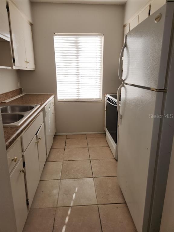 A galley kitchen features white cabinets, a double sink, a refrigerator, and tiled flooring — 5507 POKEWEED COURT UNIT C, TAMPA, FL
