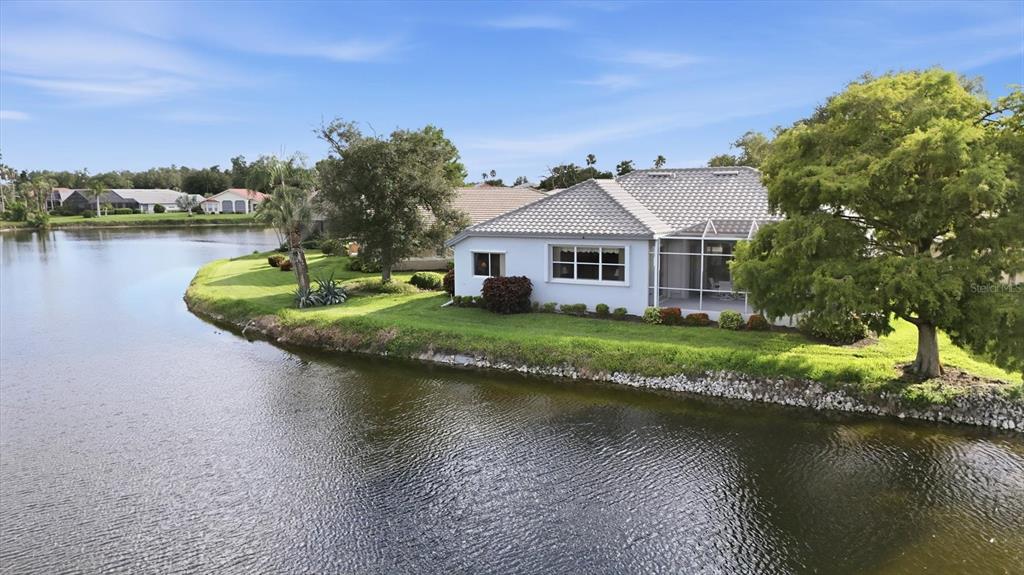 An aerial view of a single-story house situated on a grassy point along a lake — 3175 VILLAGE LANE, PORT CHARLOTTE, FL