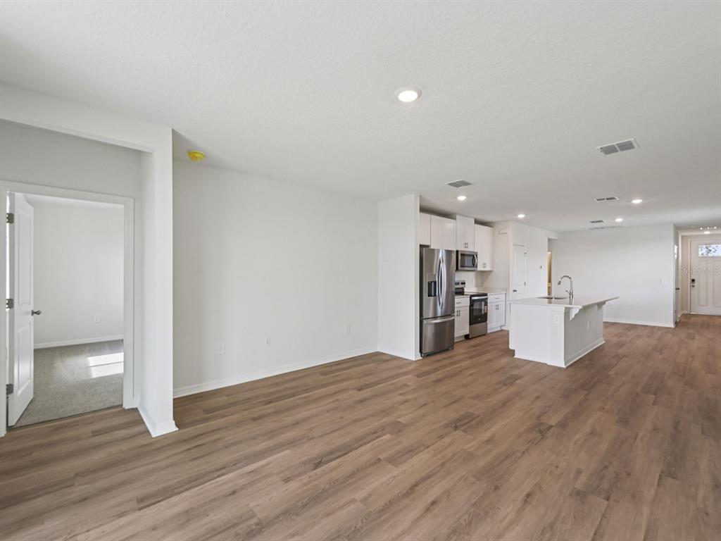 An open-concept living area features wood-look flooring, white walls, and a modern kitchen with an island — 13617 SHELLMORE AVENUE, PALMETTO, FL