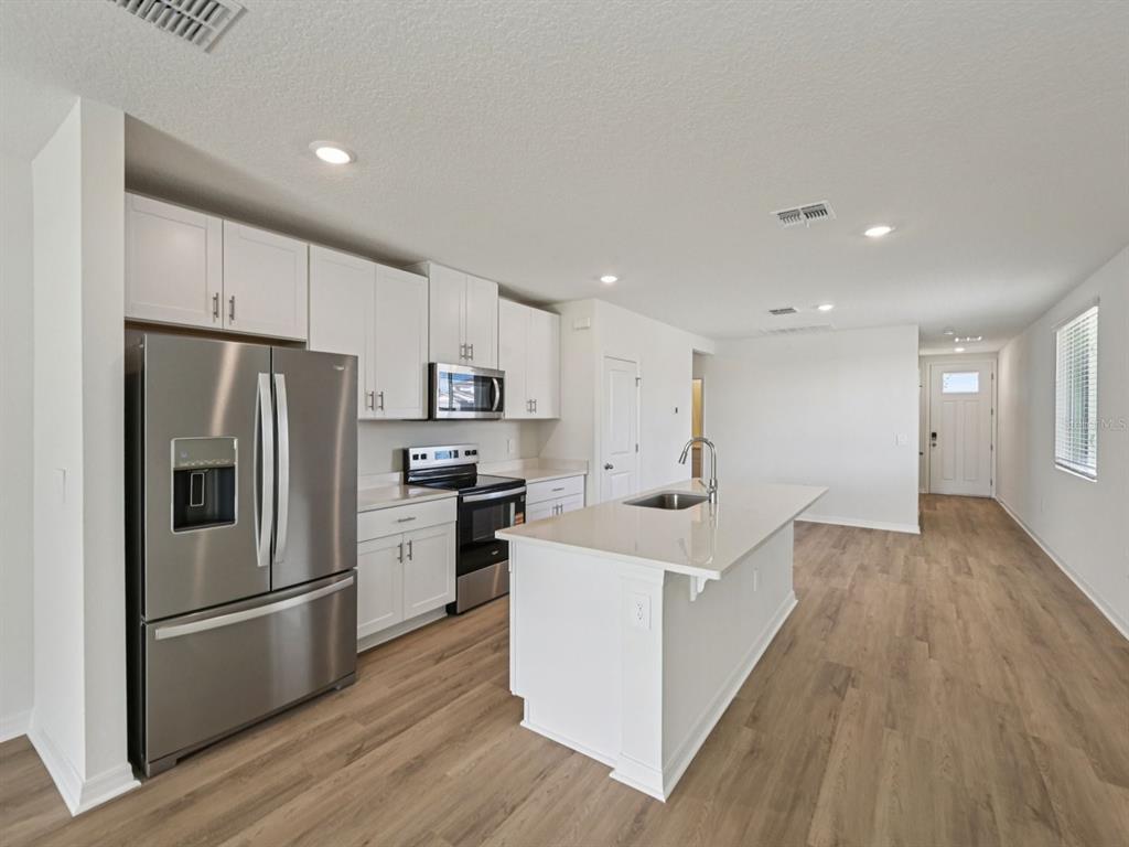 A modern kitchen features white cabinets, stainless steel appliances, and a central island with seating — 13617 SHELLMORE AVENUE, PALMETTO, FL