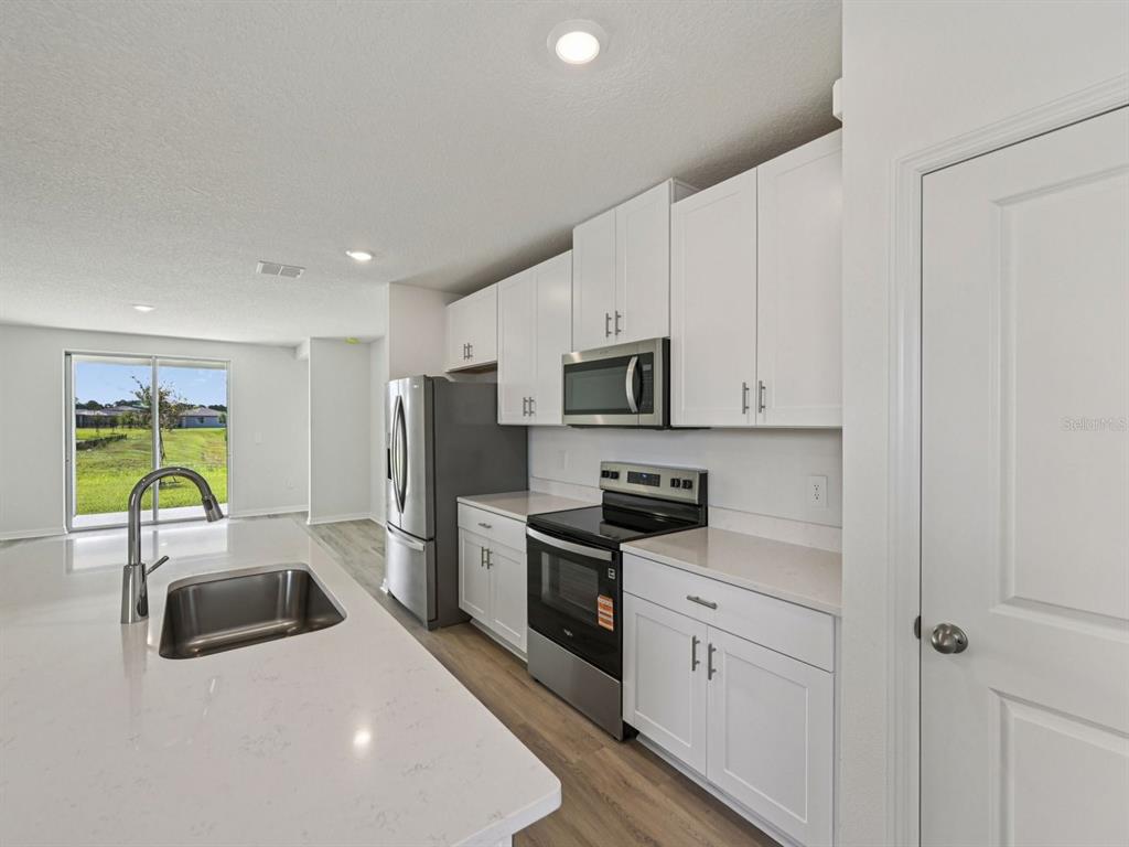A modern kitchen features white cabinets, stainless steel appliances, a quartz island, and wood flooring — 13617 SHELLMORE AVENUE, PALMETTO, FL