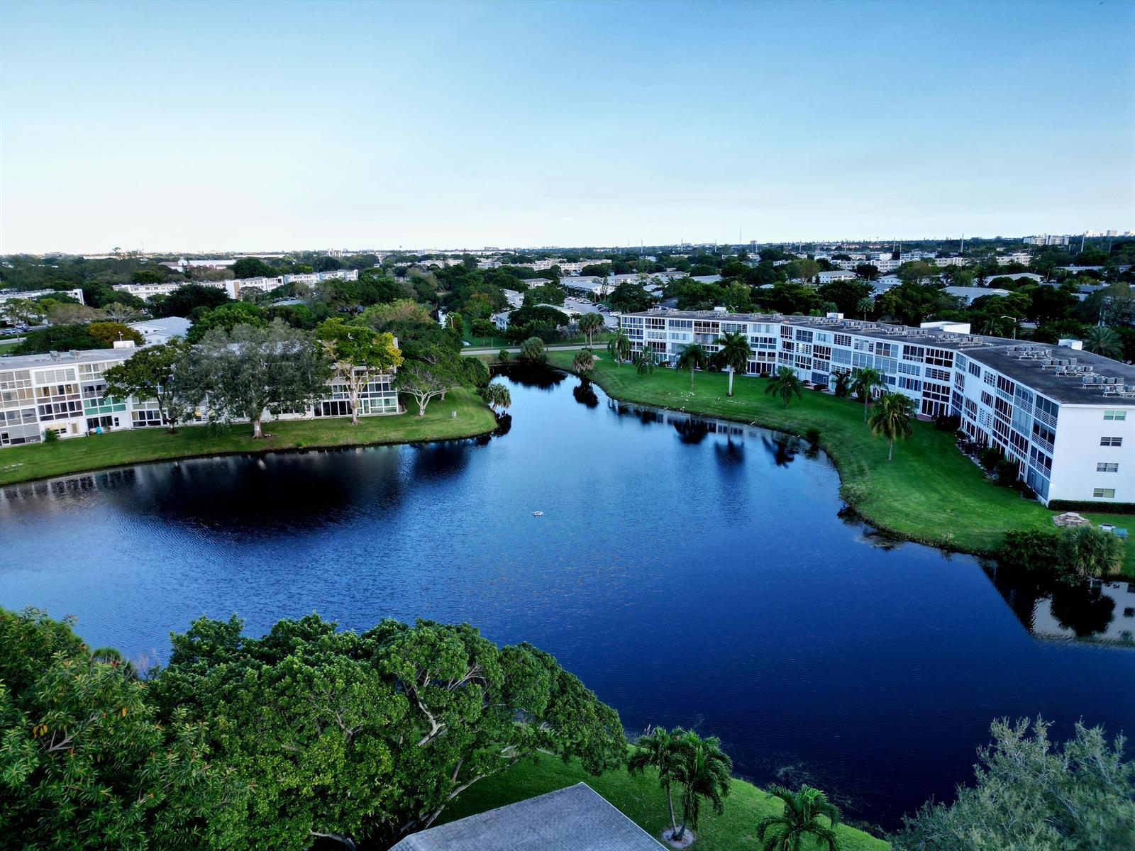 An aerial view of apartment buildings surrounding a lake with green lawns and palm trees — 144 Tilford G Place # 144, Deerfield Beach FL 33442, DEERFIELD BEACH, FL