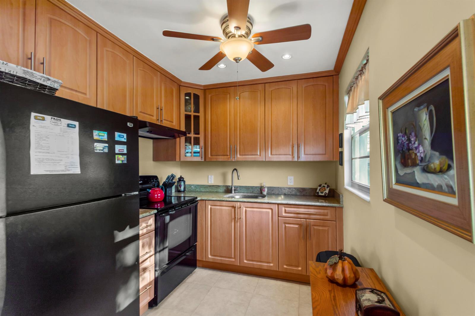 A kitchen features light wood cabinets, a black refrigerator, a stove, and a ceiling fan — 144 Tilford G Place # 144, Deerfield Beach FL 33442, DEERFIELD BEACH, FL