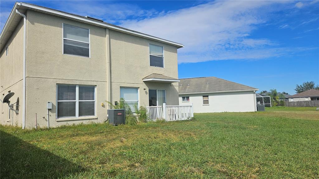 The rear exterior of a two-story beige house with a small white fenced patio area — 6836 ARAMON COURT, WESLEY CHAPEL, FL