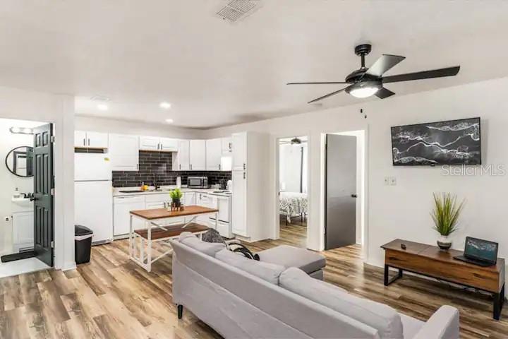 An open-concept living room and kitchen with white cabinets, dark tile backsplash, and wood flooring — 2301 CARLTON DRIVE, ORLANDO, FL