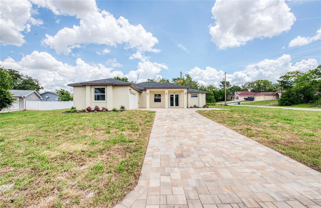 A single-story house with a paved driveway and a light-colored exterior under a cloudy sky — 12027 VILLA ROAD, SPRING HILL, FL