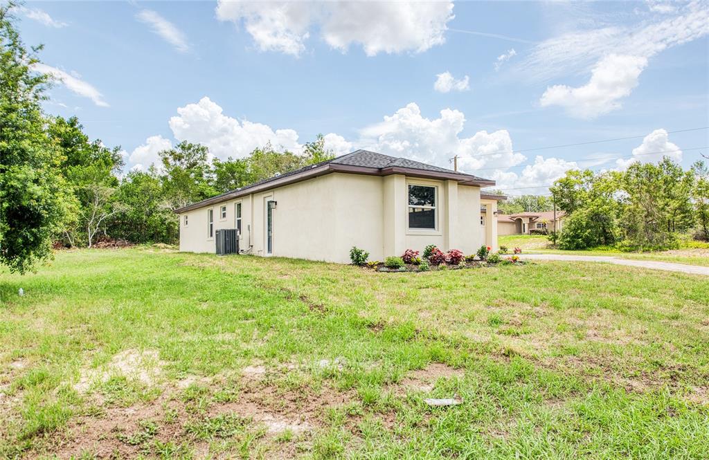 A side view of a single-story house with a beige stucco exterior and grass yard — 12027 VILLA ROAD, SPRING HILL, FL