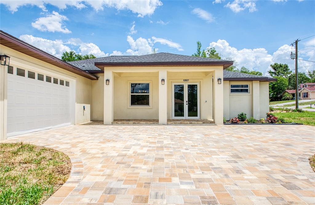 A single-story house exterior features a paved driveway, a covered porch, and a white garage — 12027 VILLA ROAD, SPRING HILL, FL
