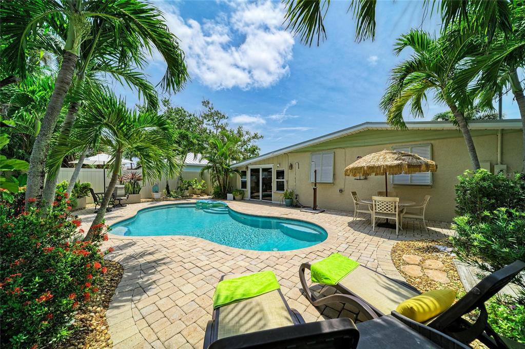 A backyard features a swimming pool, brick paver patio, lounge chairs, and tropical landscaping — 2711 AVENUE C, HOLMES BEACH, FL
