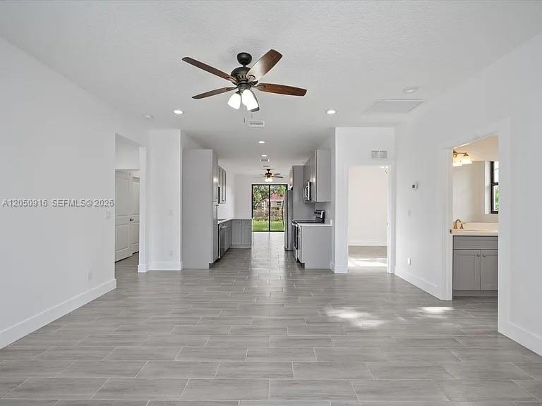 An open-concept living area features gray tile flooring, white walls, and a modern kitchen — 141 W 16th St, Riviera Beach FL 33404, RIVIERA BEACH, FL