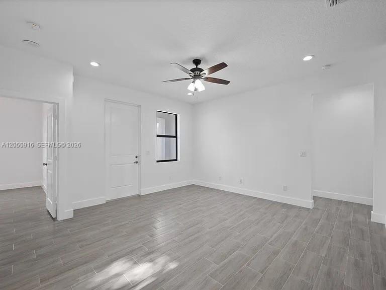 A bright, empty room features white walls, gray wood-look tile flooring, and a ceiling fan — 141 W 16th St, Riviera Beach FL 33404, RIVIERA BEACH, FL