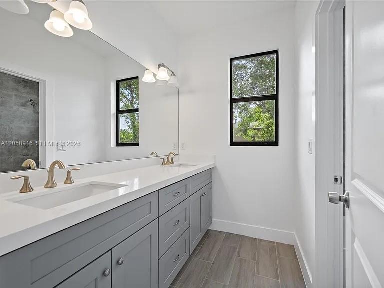 A modern bathroom features a gray double vanity, large mirror, and wood-look tile flooring — 141 W 16th St, Riviera Beach FL 33404, RIVIERA BEACH, FL