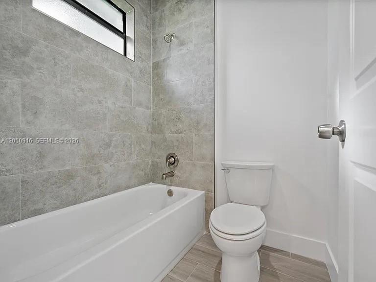 A bathroom features a white bathtub, a toilet, and gray tiled walls — 141 W 16th St, Riviera Beach FL 33404, RIVIERA BEACH, FL