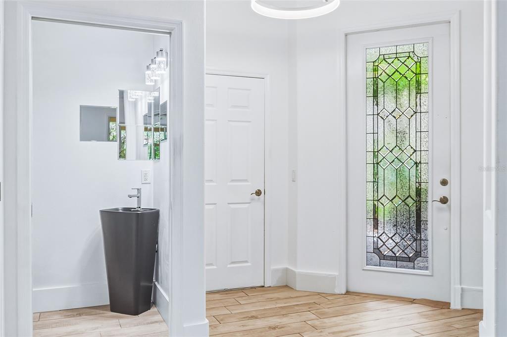A bright entryway features a modern pedestal sink, white walls, wood-look tile, and a glass-paneled door — 3663 SQUARE WEST LANE UNIT 12, SARASOTA, FL