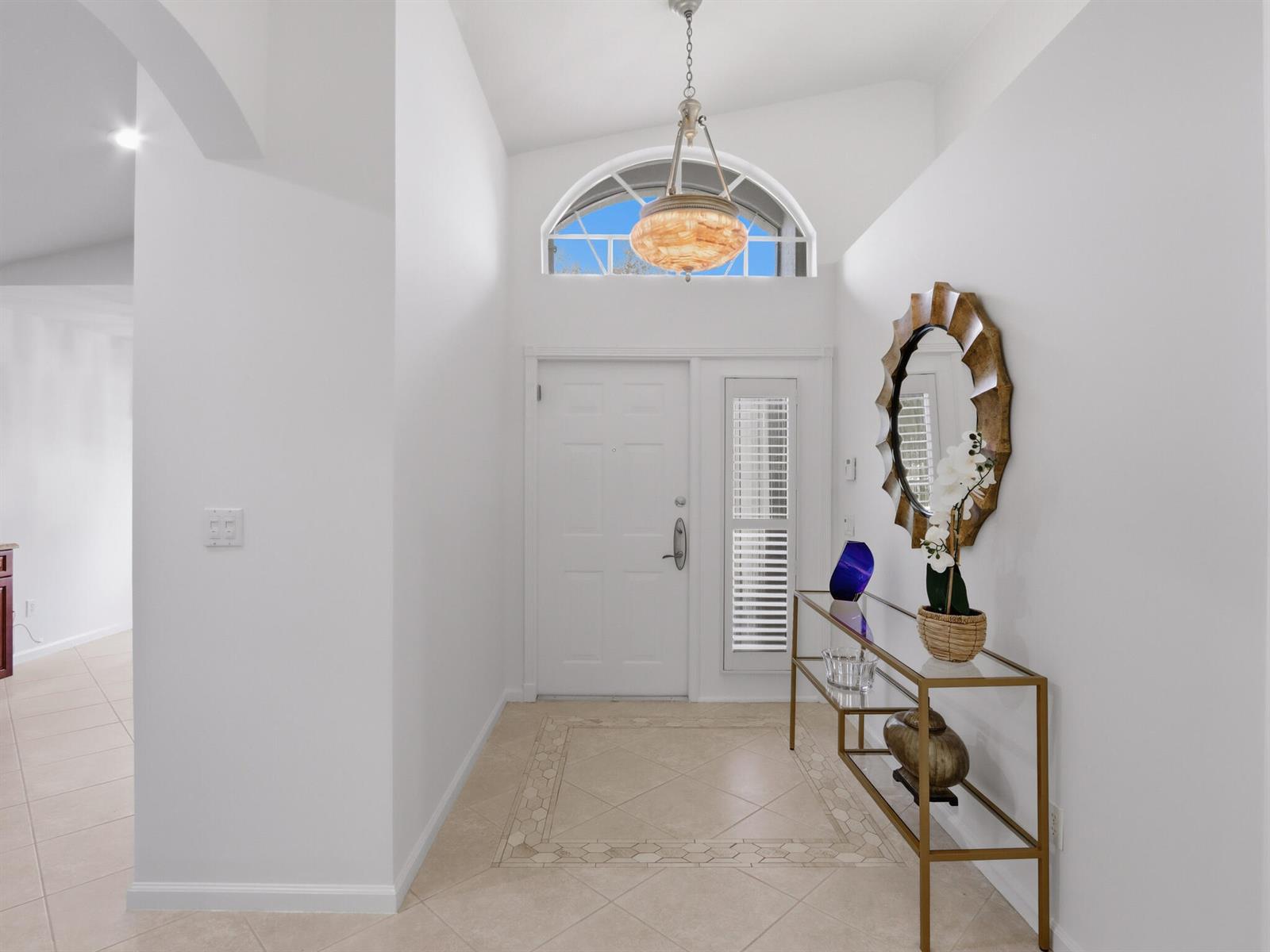 A bright entryway features a glass console table, a round mirror, and a vaulted ceiling — 11184 Ihilani Way, Boynton Beach FL 33437, BOYNTON BEACH, FL