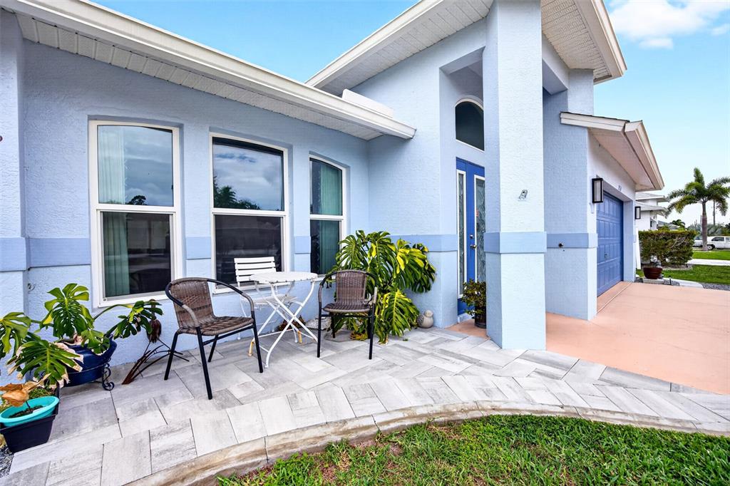 A light blue house exterior features a paved patio, two chairs, and a small table — 25652 AYSEN DRIVE, PUNTA GORDA, FL