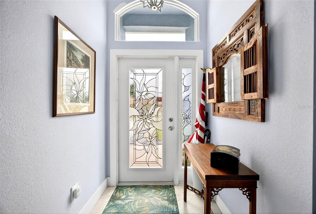 An entryway features a white door with floral glass, a wooden console table, and a mirror — 25652 AYSEN DRIVE, PUNTA GORDA, FL