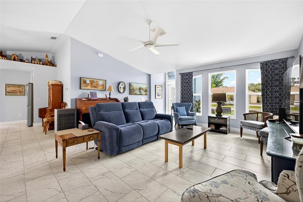 A living room features a blue sofa, tile flooring, a vaulted ceiling, and large windows — 25652 AYSEN DRIVE, PUNTA GORDA, FL