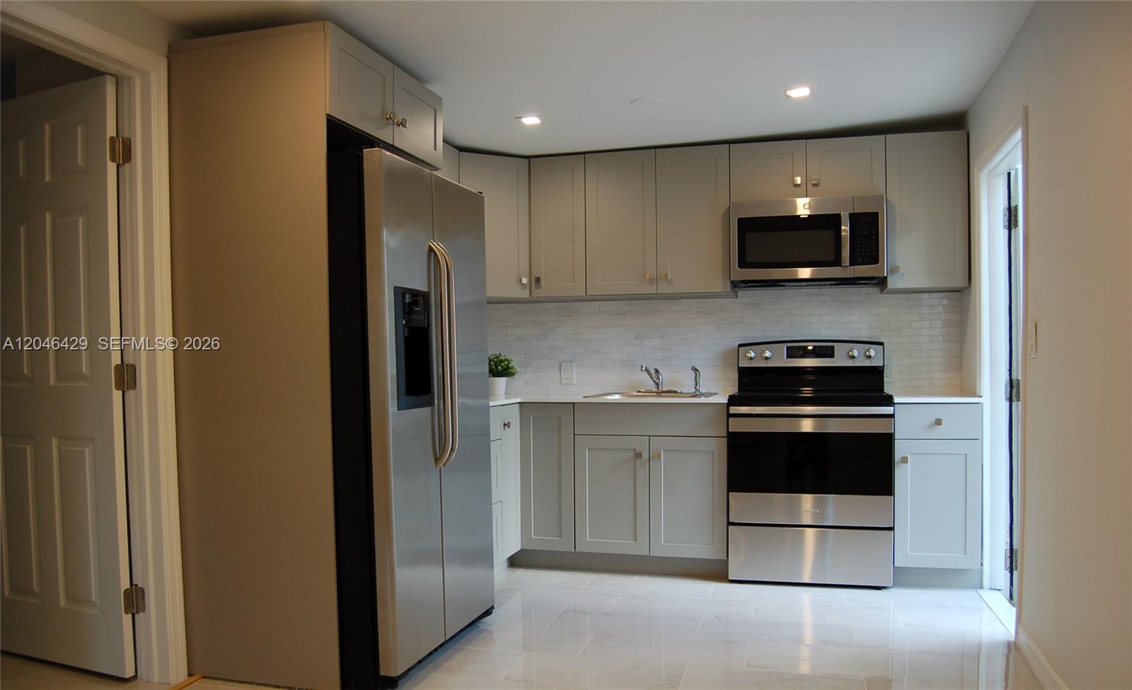 A kitchen features grey cabinets, stainless steel appliances, white countertops, and a tiled backsplash — MIAMI, FL