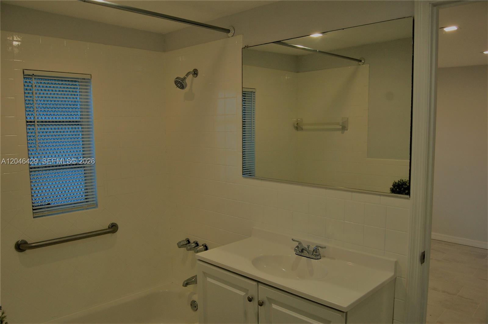 A bathroom features a white vanity, a large wall mirror, and a tiled shower-tub combination — MIAMI, FL