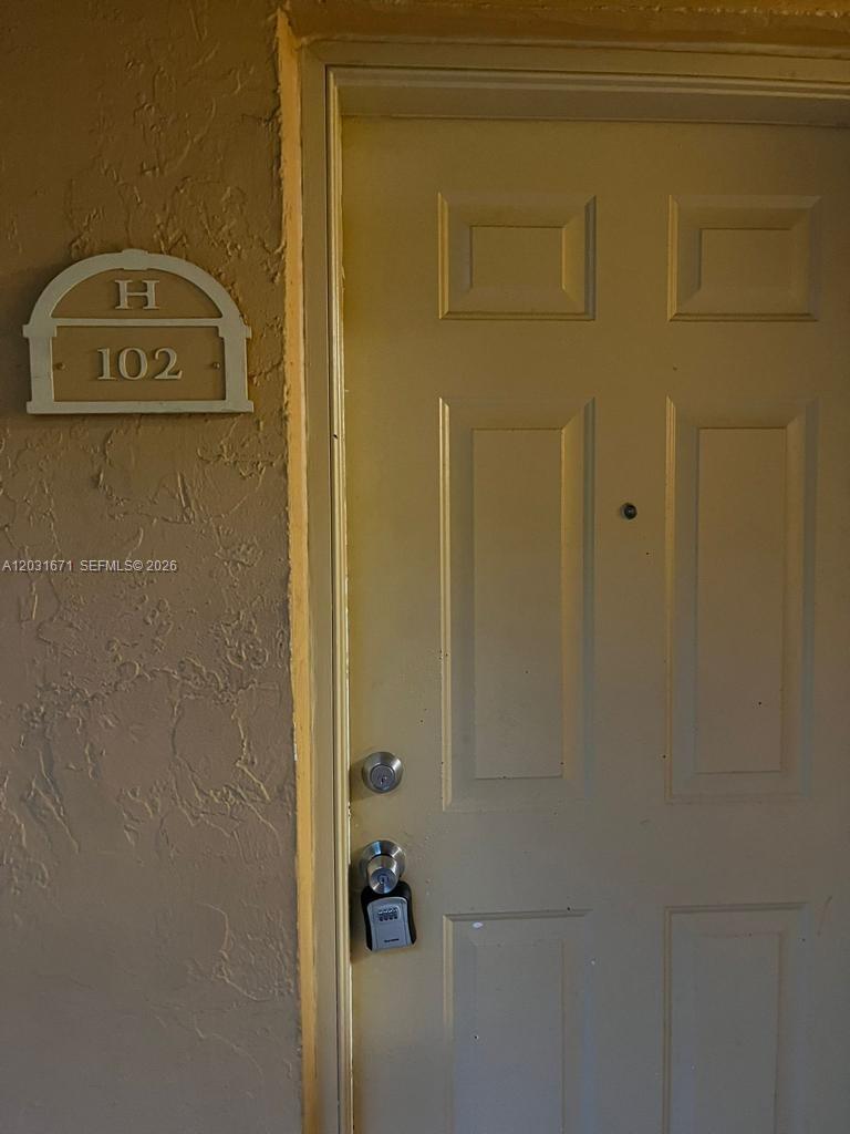A beige door with a lockbox and a unit number sign labeled H 102 — 18111 NW 68th Ave # H102, Hialeah FL 33015, HIALEAH, FL