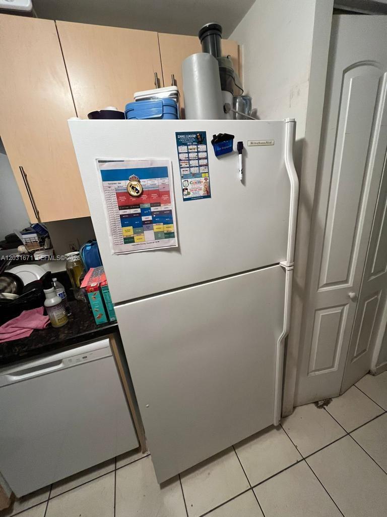 A white top-freezer refrigerator stands in a kitchen with light wood cabinets and tile flooring — 18111 NW 68th Ave # H102, Hialeah FL 33015, HIALEAH, FL