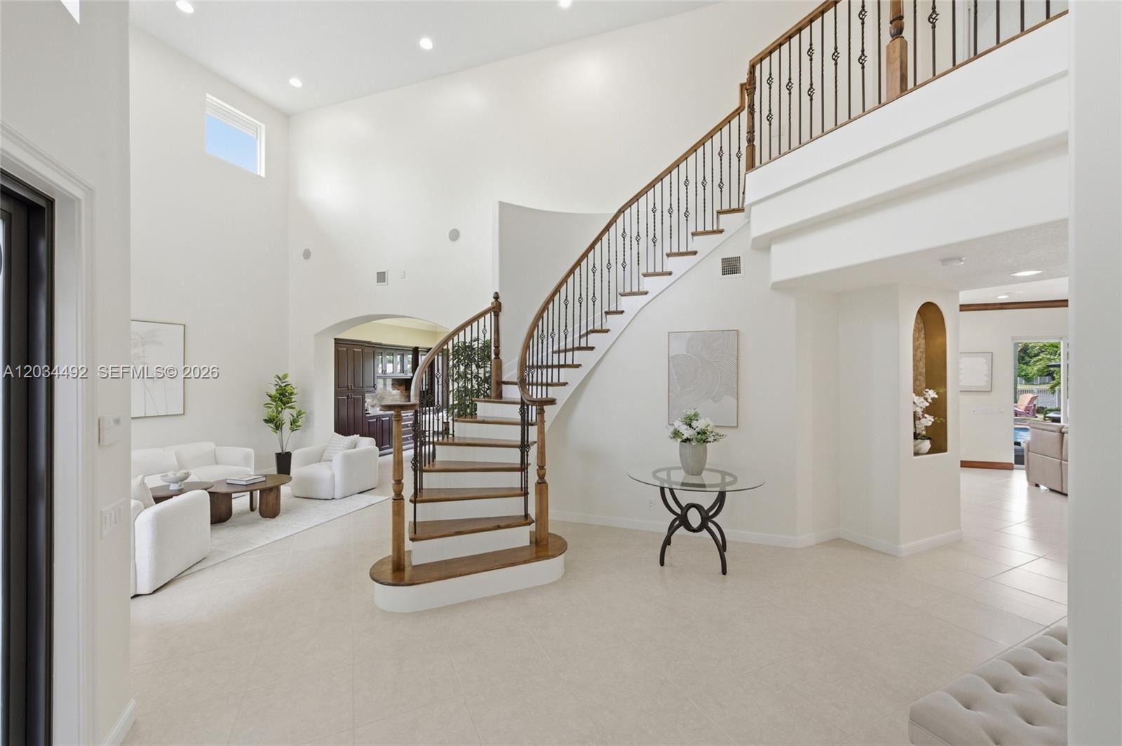A grand foyer features a curved wooden staircase with iron railings and white tile flooring — 929 Gulfstream Ct, Weston FL 33327, WESTON, FL