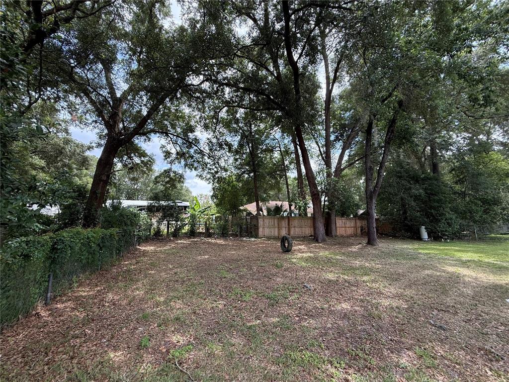 A grassy backyard features several large trees, a wooden fence, and a tire swing — 4600 SE 136TH LANE, SUMMERFIELD, FL