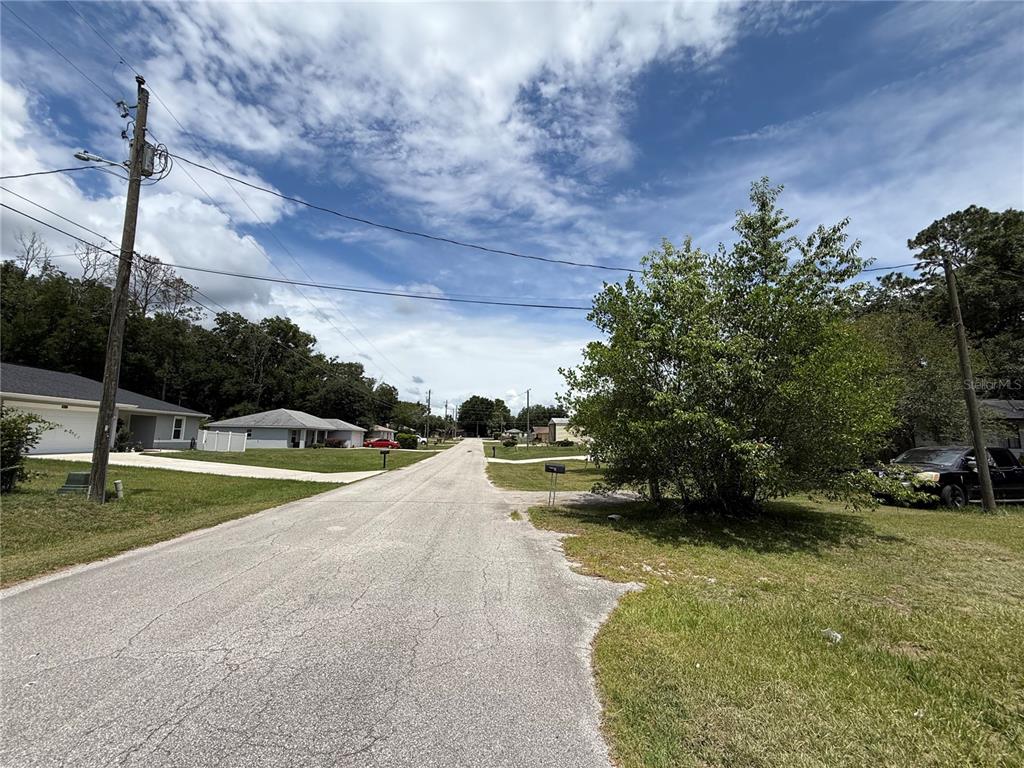 A paved residential street lined with houses, trees, and utility poles under a cloudy sky — 4600 SE 136TH LANE, SUMMERFIELD, FL