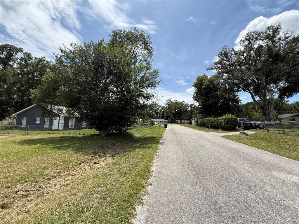 A paved road leads past a grey house and trees under a blue sky — 4600 SE 136TH LANE, SUMMERFIELD, FL