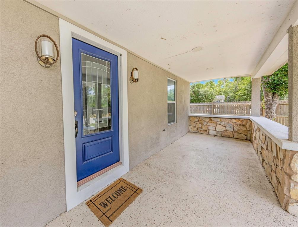 A covered front porch features a blue door, stone accents, and a concrete floor — 9224 ELZA STREET, NEW PORT RICHEY, FL
