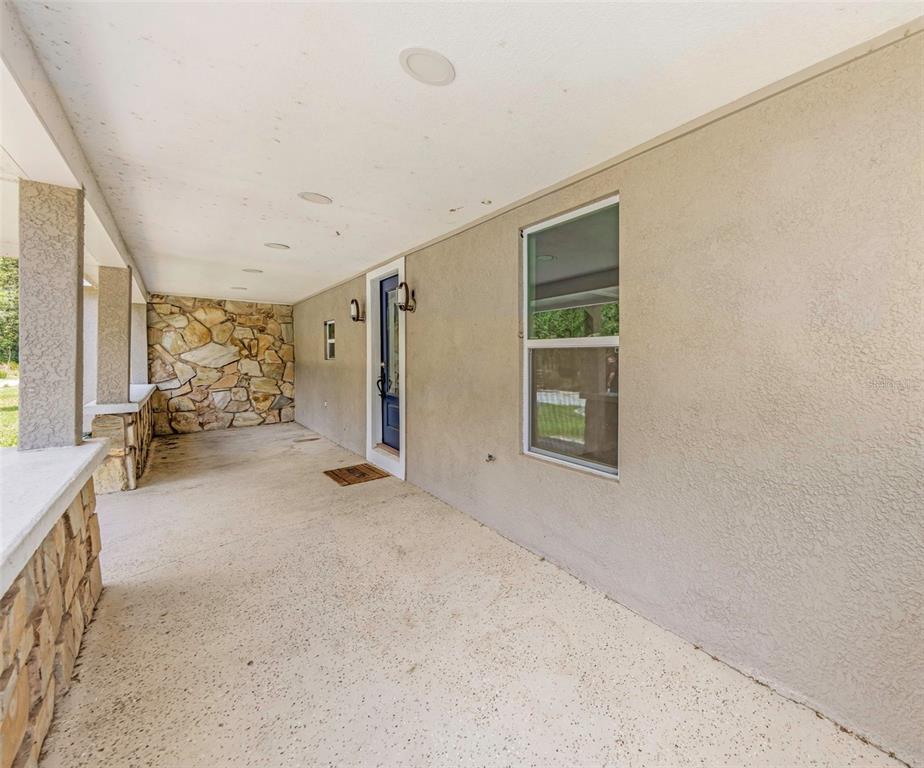 A covered front porch features a stone accent wall, a blue door, and concrete flooring — 9224 ELZA STREET, NEW PORT RICHEY, FL