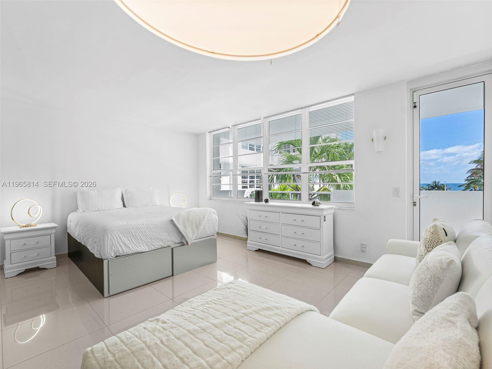 A bright bedroom features a bed, dresser, sofa, and a balcony door overlooking the ocean — 100 Lincoln Rd # 417, Miami Beach FL 33139, MIAMI BEACH, FL