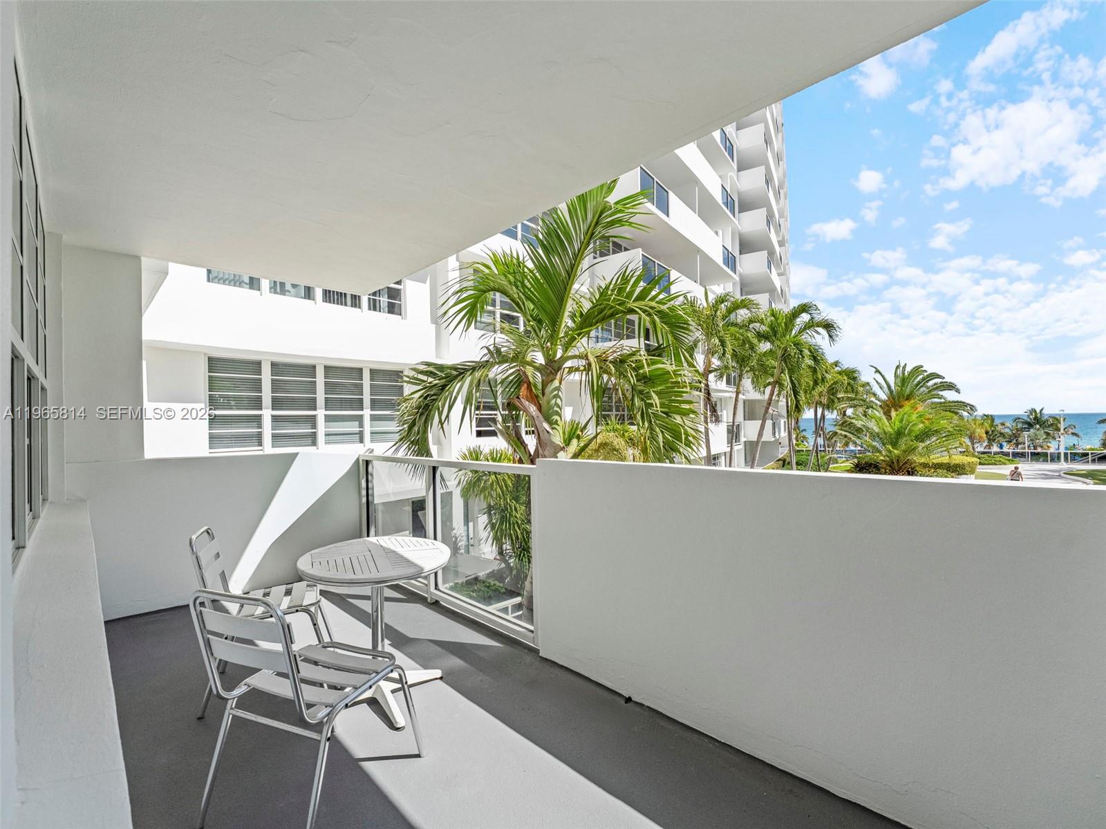 A balcony with a small table and two chairs overlooks palm trees and the ocean — 100 Lincoln Rd # 417, Miami Beach FL 33139, MIAMI BEACH, FL