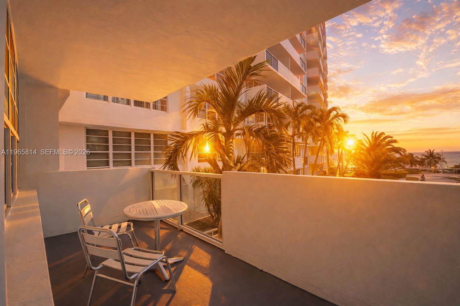 A balcony with a small table and two chairs overlooks palm trees at sunset — 100 Lincoln Rd # 417, Miami Beach FL 33139, MIAMI BEACH, FL