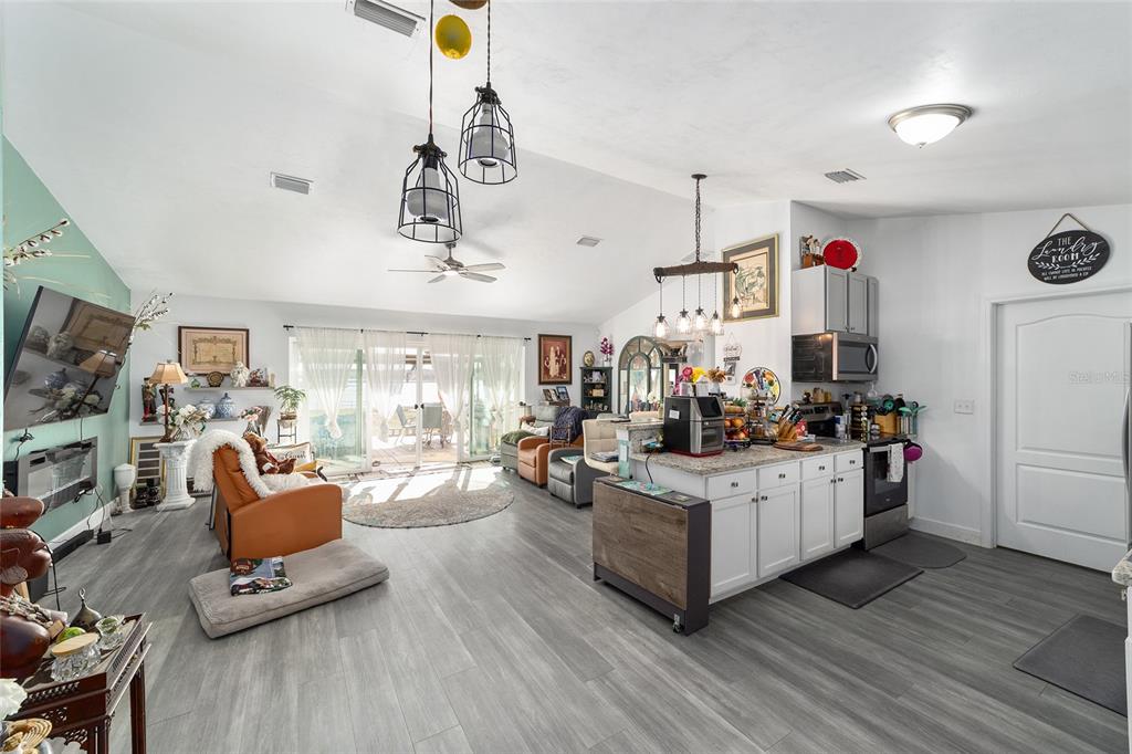 An open-concept living area features gray wood-look flooring, a kitchen island, and sliding glass doors — 2120 SE 41ST WAY, TRENTON, FL