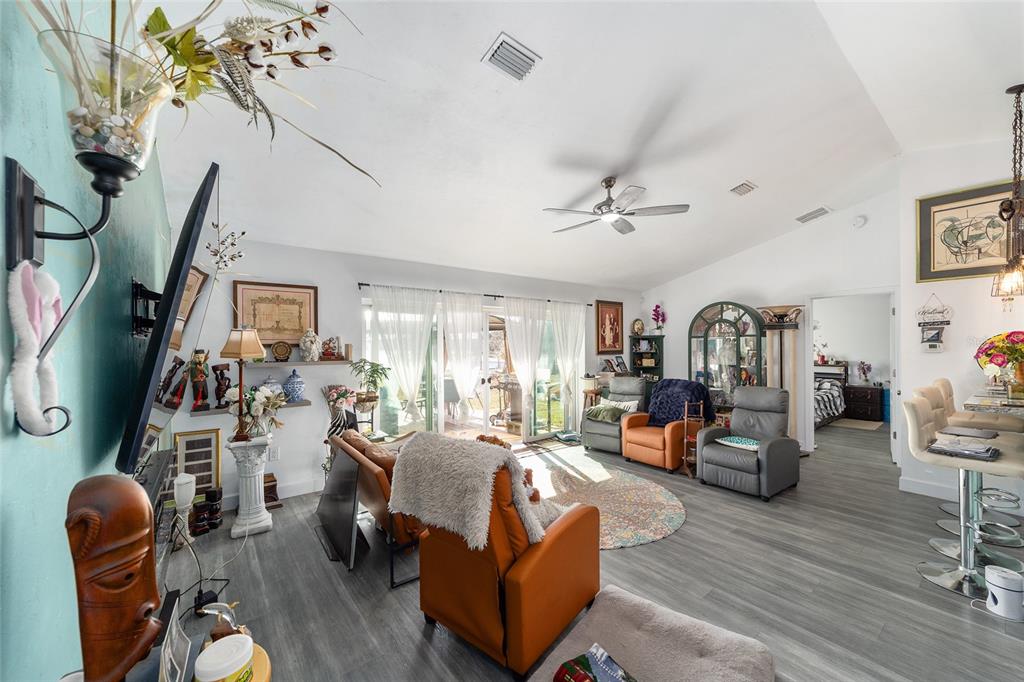 A living room features gray wood-look flooring, vaulted ceilings, a ceiling fan, and sliding doors — 2120 SE 41ST WAY, TRENTON, FL