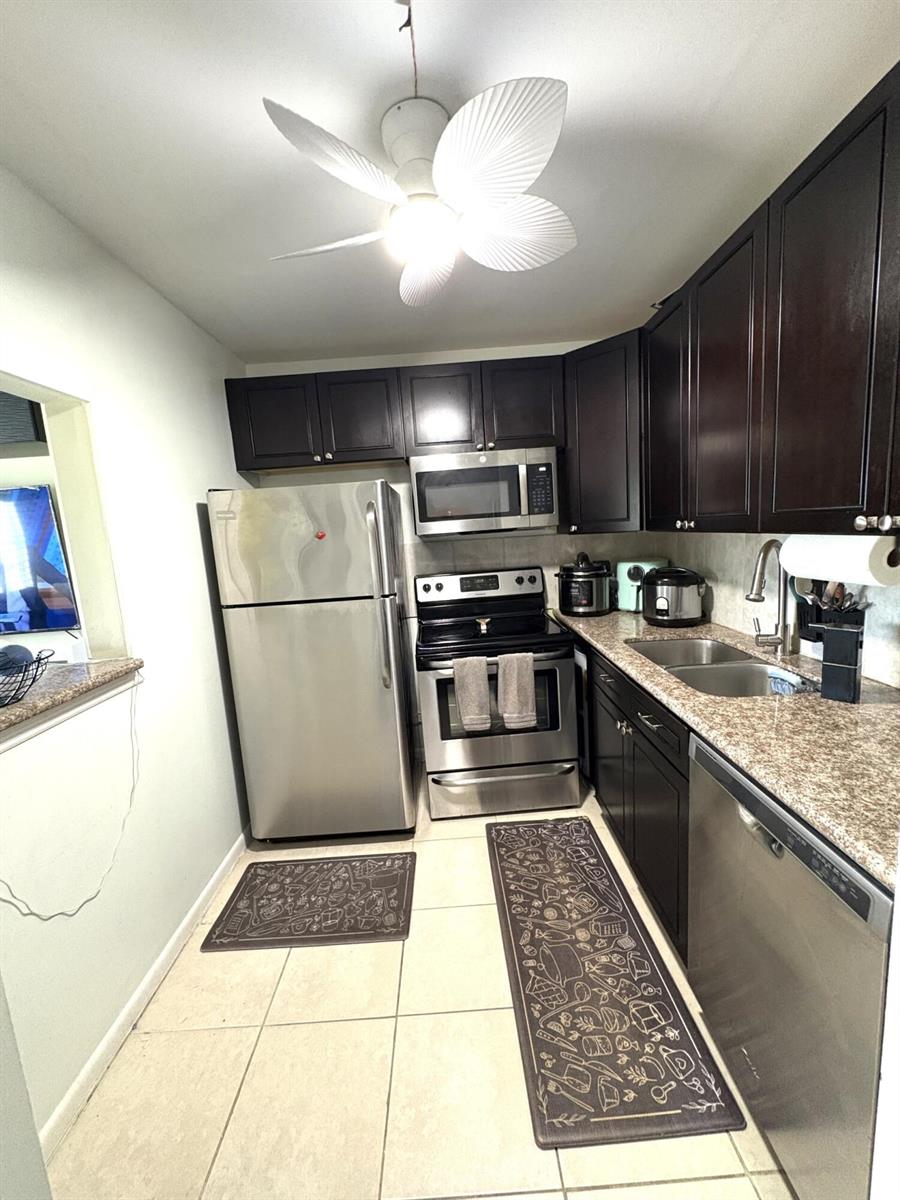 A kitchen features dark wood cabinets, stainless steel appliances, granite countertops, and tile flooring — 65 Preston B, Boca Raton FL 33434, BOCA RATON, FL